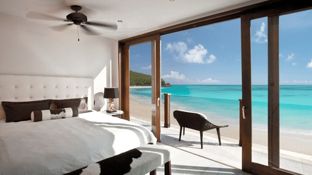 A spacious bedroom with a large bed opens up to a stunning ocean view through expansive glass doors.