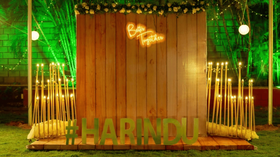 Rustic wooden photo backdrop with the couple's initials and name ‘Harindu’ in glowing lights at Ilara Hotels & Spa, OMR, Chennai