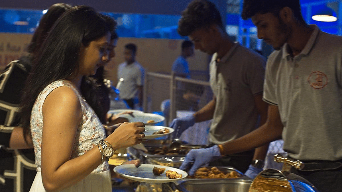 People serving themselves food from a buffet table with plates and chafing dishes.
