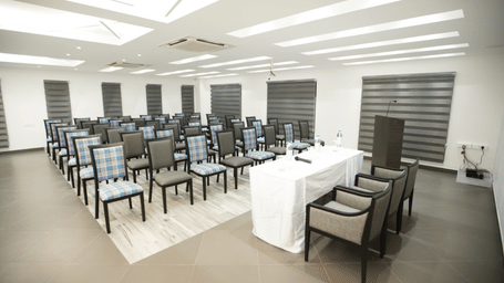 A spacious, well-lit hall with neatly arranged chairs in classroom style and large windows | Regency Palani by GRT Hotels