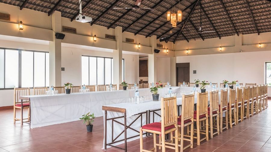 The airy and open dining hall at Forest Escapes Koyna features long tables and chairs, with natural light streaming in.