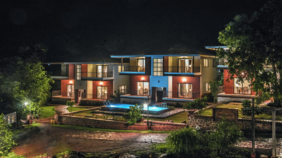 Night view of a beautifully lit resort with modern architecture, a central pool, and lush greenery.