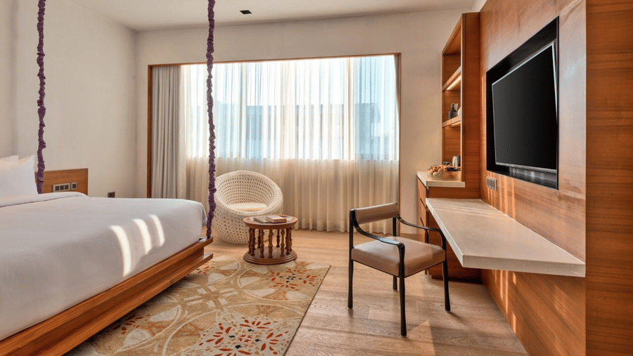 Hotel room in South Goa with wooden interiors, furniture and a white bed that offers in-room massage