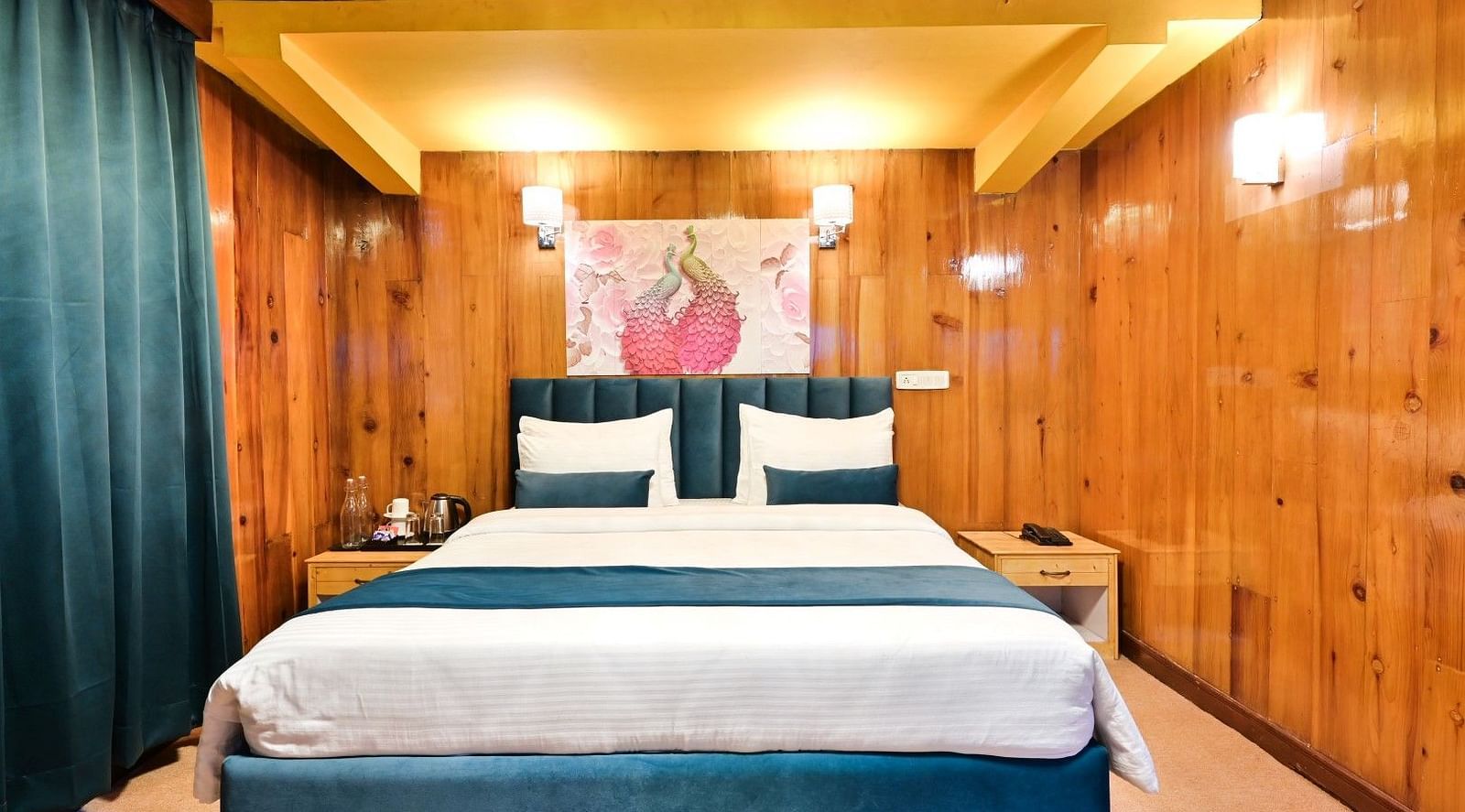 A cosy hotel room with a comfortable bed, wooden walls, and a painting above the headboard.