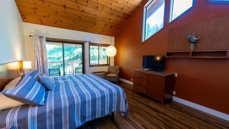 A Deluxe King Room at Amador Hotel with a wooden ceiling, a king-sized bed with striped bedding, and a TV on a dresser.