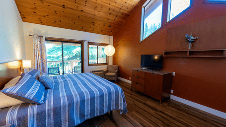 A Deluxe King Room at Amador Hotel, offering accommodation near Kirkwood, featuring a wooden ceiling, a king size bed with striped bedding, and a TV on a dresser.