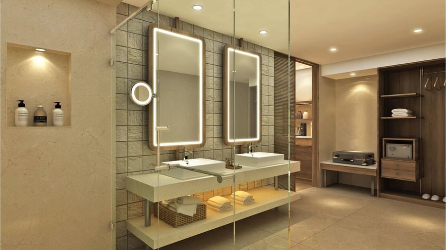 Bathroom at Haveloook Water Villa in Symphony Palms Beach Resort and Spa featuring huge mirrors with lights on the wall, wash basins below them and under them there are towels and bathrobe placed. There are also other items present in shelves like shampoo,