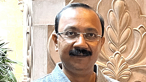 Bijitendra Mittra in a grey polo shirt standing in front of a carved stone wall, smiling at the camera.