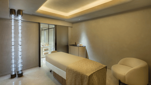 Therapy room at Aavraa Wellness of The Residency Towers Chennai featuring a massage bed with a couch next to it and a table next to the way to the washroom