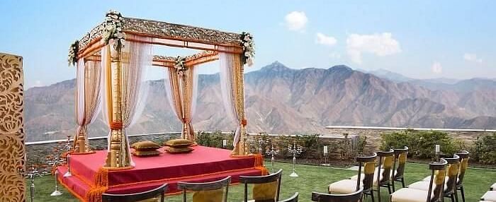 a mandap set up meant for wedding ceremony on manicured lawn with chairs facing it and in the background there are hils at a distance- neer ganga Resorts
