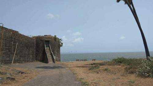 A stone gateway of a fort near the coastline with a palm tree and pathway leading to the sea.