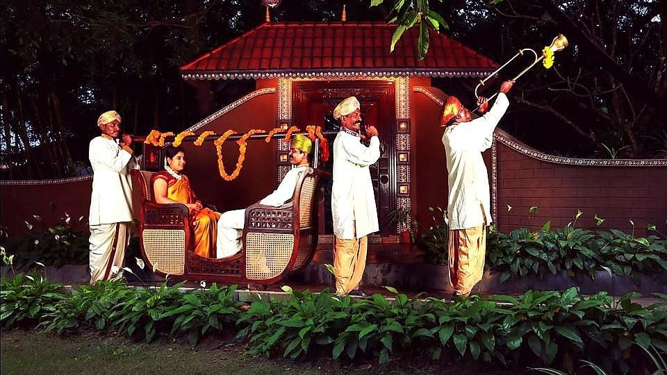 A couple in a traditional palanquin, escorted by musicians and attendants in a festive procession - Hoysala Village Resort