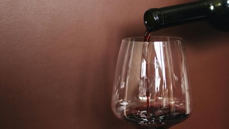 Red wine being elegantly poured into a clear glass against a rich burgundy background.