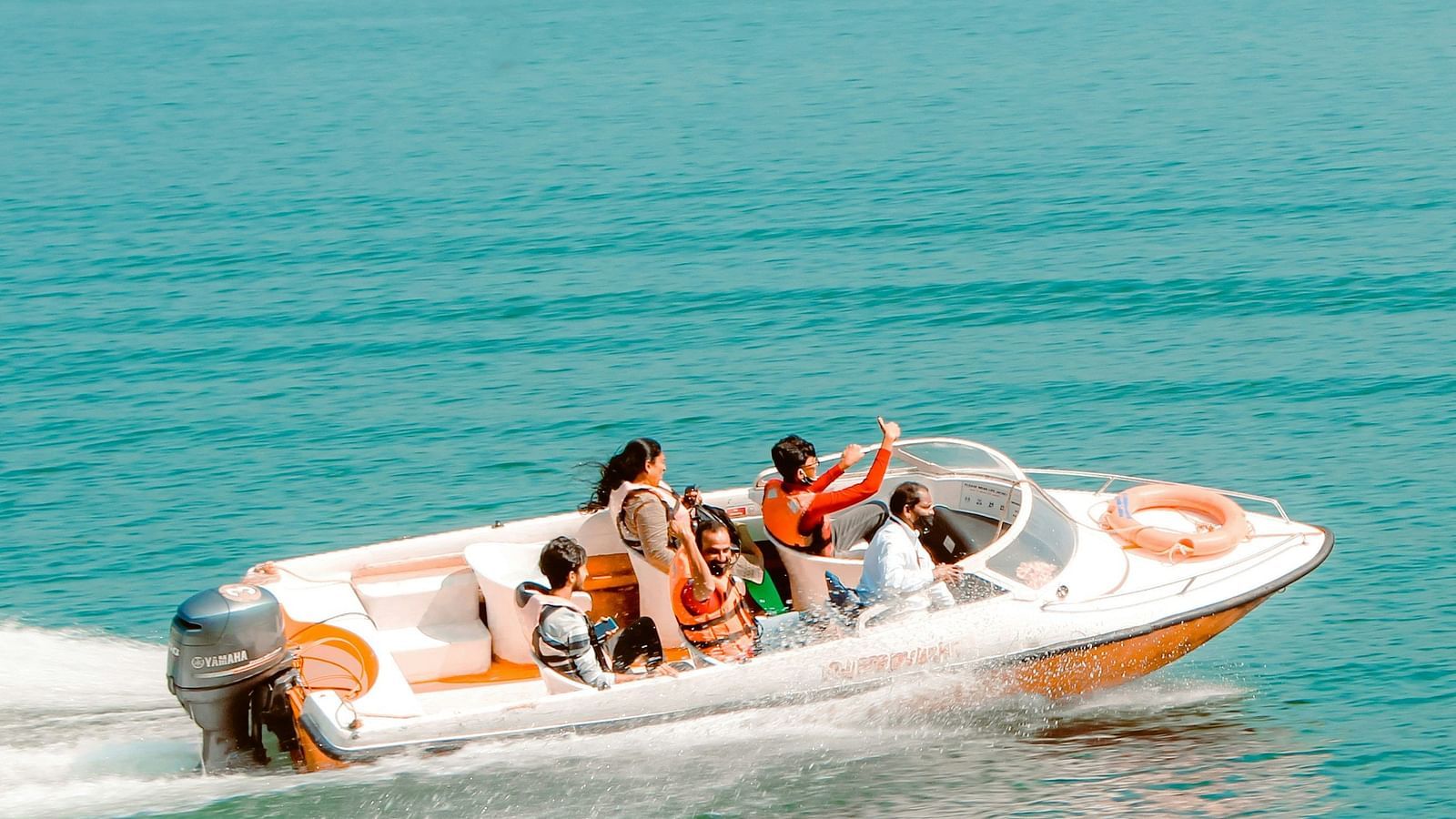 A group of people enjoying a thrilling speedboat ride on turquoise waters, with lush green hills in the background.