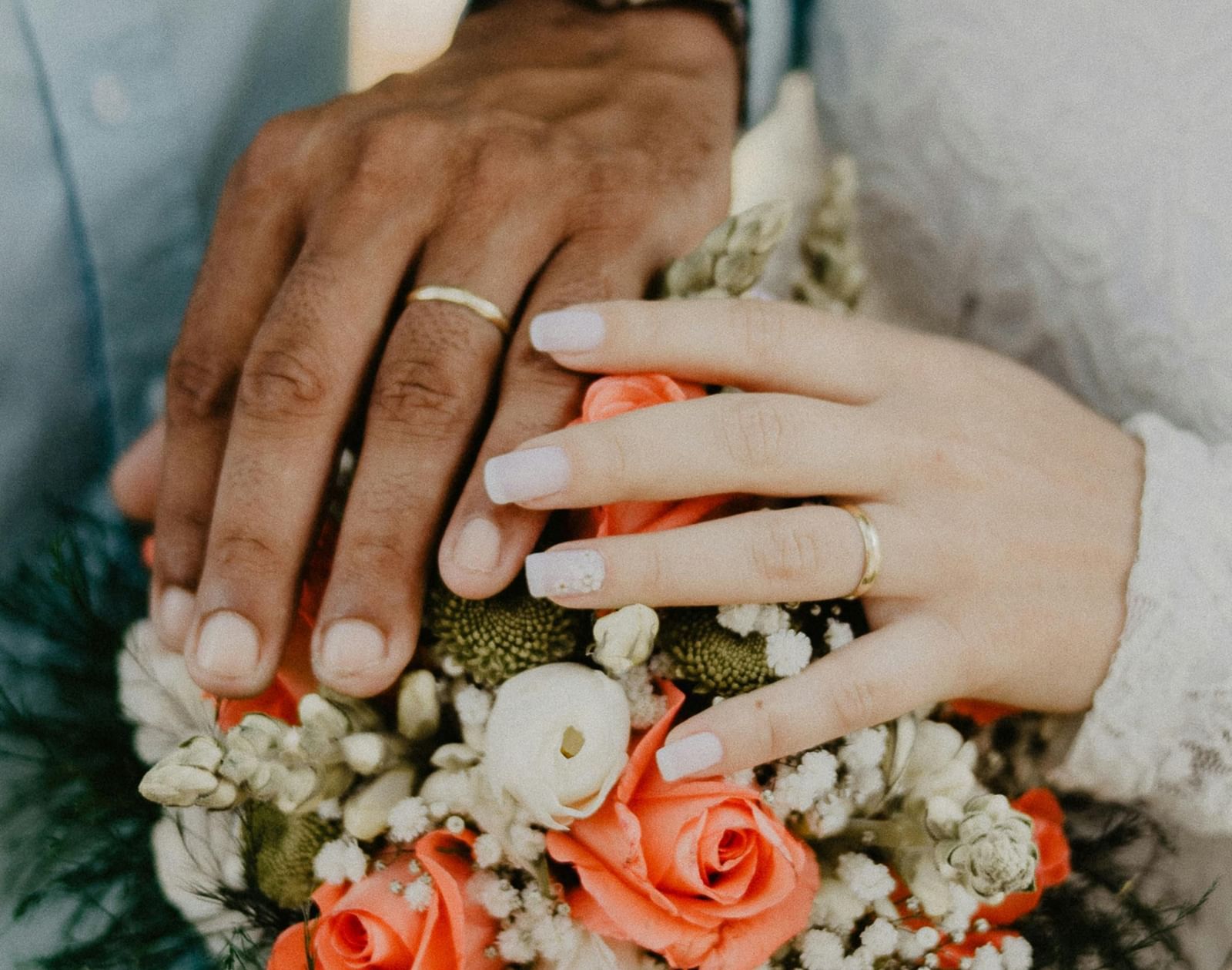 A couple wearing rings, and their hands holding a flower bouquet together at Tallman Hotel.