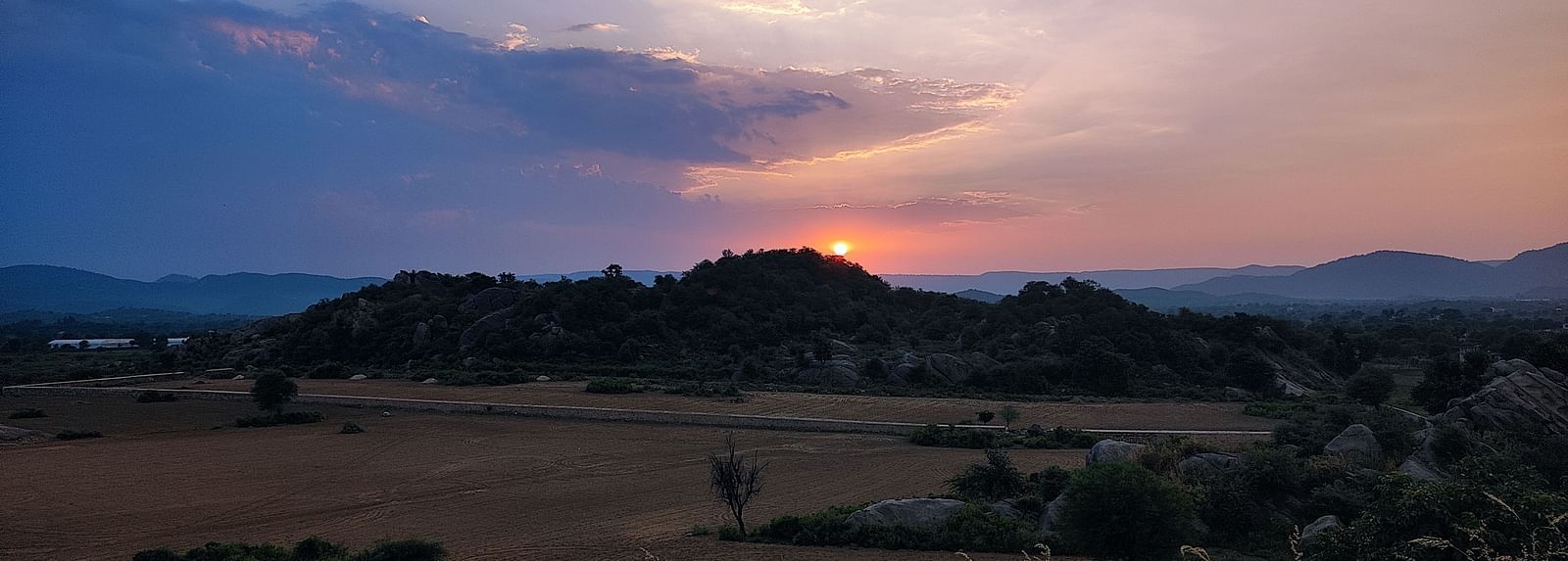 A picture featuring a range of mountains and sunset, with both dry and green land