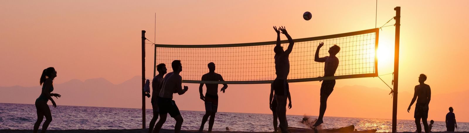 An image of group of friends enjoying volleyball by the beach during a sunset