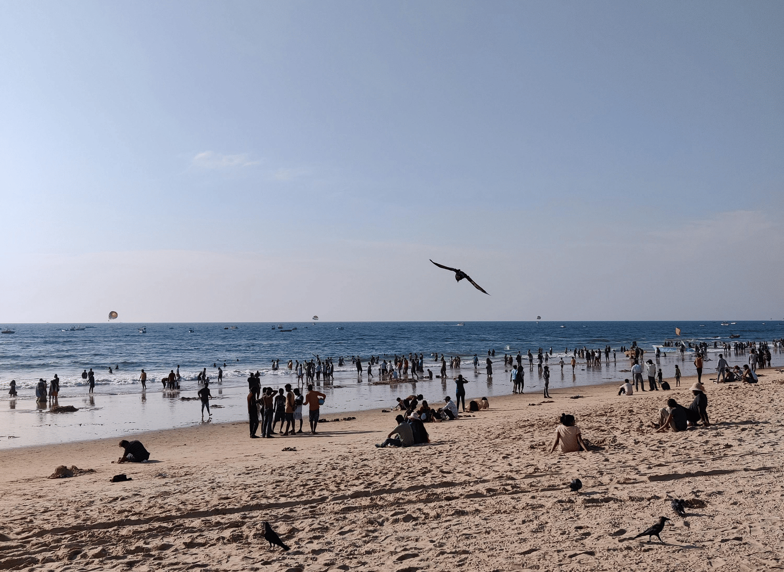 A wide expanse of a sunny, sandy beach is sparsely populated with sunbathers and distant ocean waves.