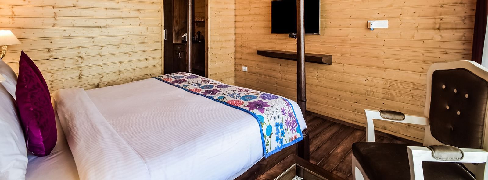 A cosy room with wood-paneled walls, a bed, a mounted TV, and an air conditioner.- Bamboo Saa Resort & Spa, Udaipur