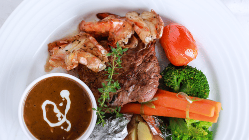 A plated dish with dark meat, assorted vegetables, and a glossy sauce is presented on a white plate.