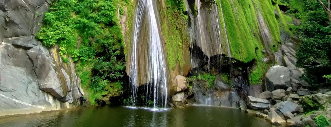 Bheel Beri Waterfalls in Rajasthan featuring water cascading down the rocky mountain surrounded by plants. At the bottom there is a pond where water gets collected.