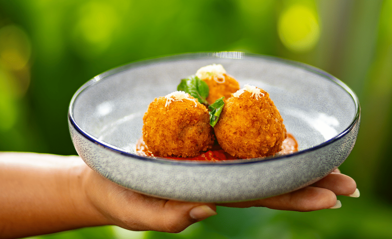 A person holds a plate with three fried, golden-brown appetisers on a bed of red sauce at Stanley Revelation.