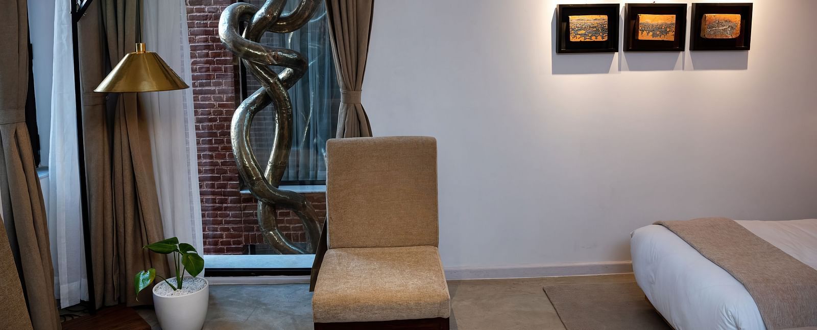 A room with a bed, chair, lamp, three pieces of art work hung on the wall, and a window overlooking the infinity loop - The Nanee