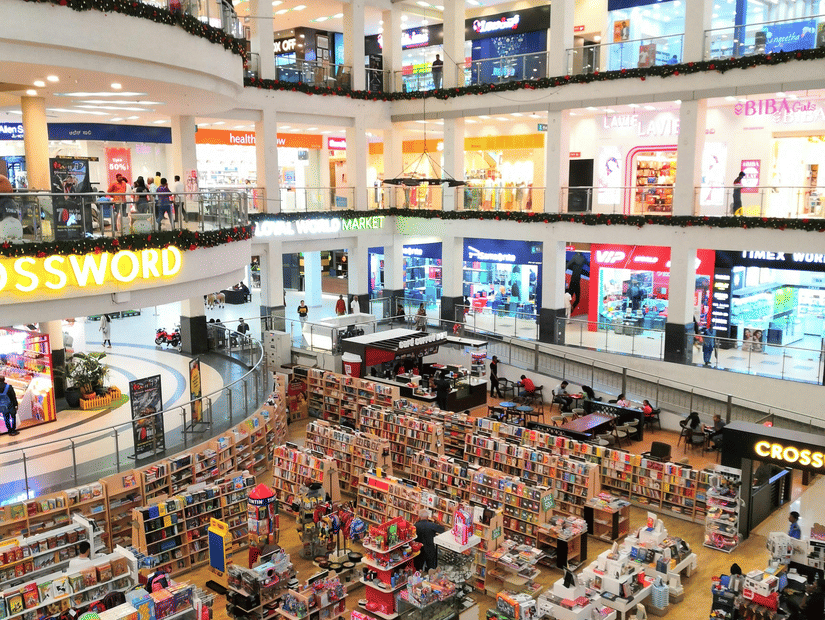 A high-angle view of a multi-storey shopping centre with bright storefronts and a busy ground floor retail area.