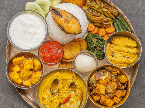 Traditional Bengali thali featuring fish curry, rice, vegetables, chutney, and classic Bengali side dishes.