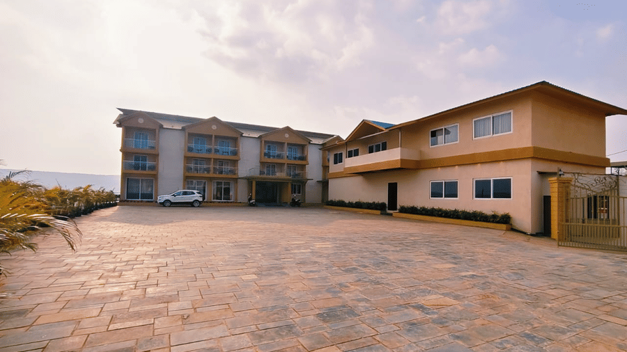 Multi-storey resort buildings stand beside a spacious paved stone driveway under a lightly clouded sky at Savyasaachii Hotel.