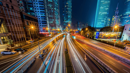 City street at night with bright light trails from traffic, representing urban nightlife, speed, and vibrant energy.