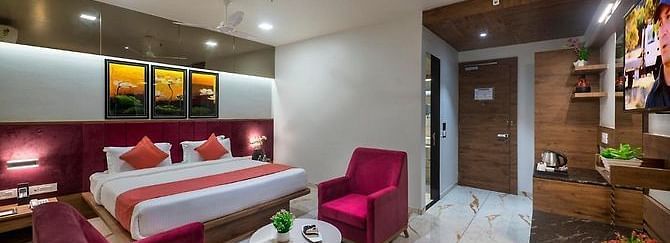A room featuring a neatly made bed, a seating area, and a dressing table at Angel Lords Eco Inn Amreli.