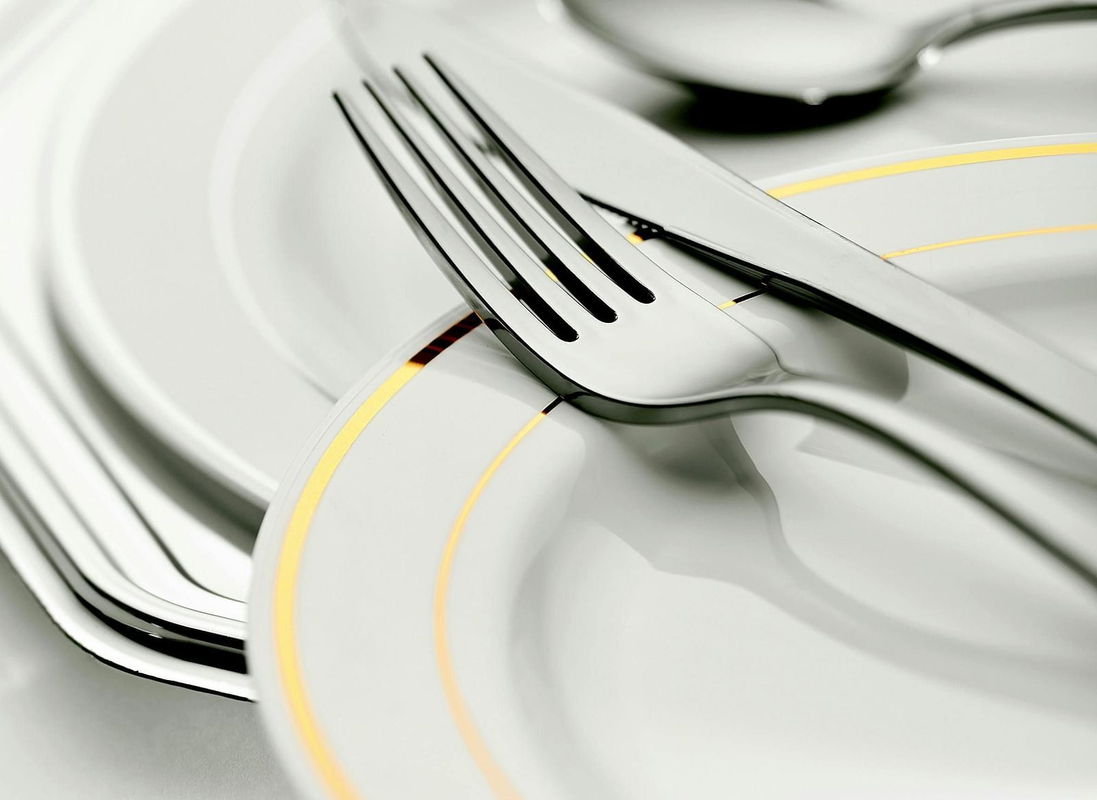A stack of white plates with a silver fork and spoon placed on top.