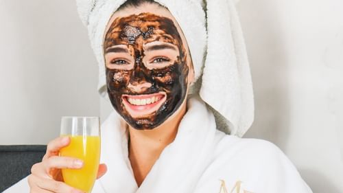 a woman with a face mask in bathrobe holding a glass of juice 