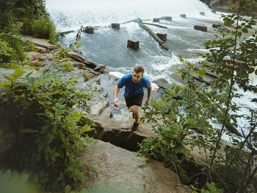 A person climbing a rocky terrain with a waterfall in view in the background.