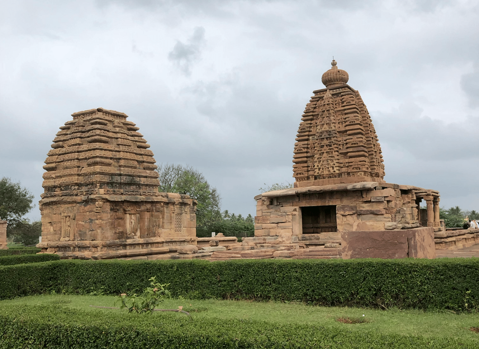Ancient stone temples surrounded by greenery, showcasing intricate architecture under a cloudy sky.