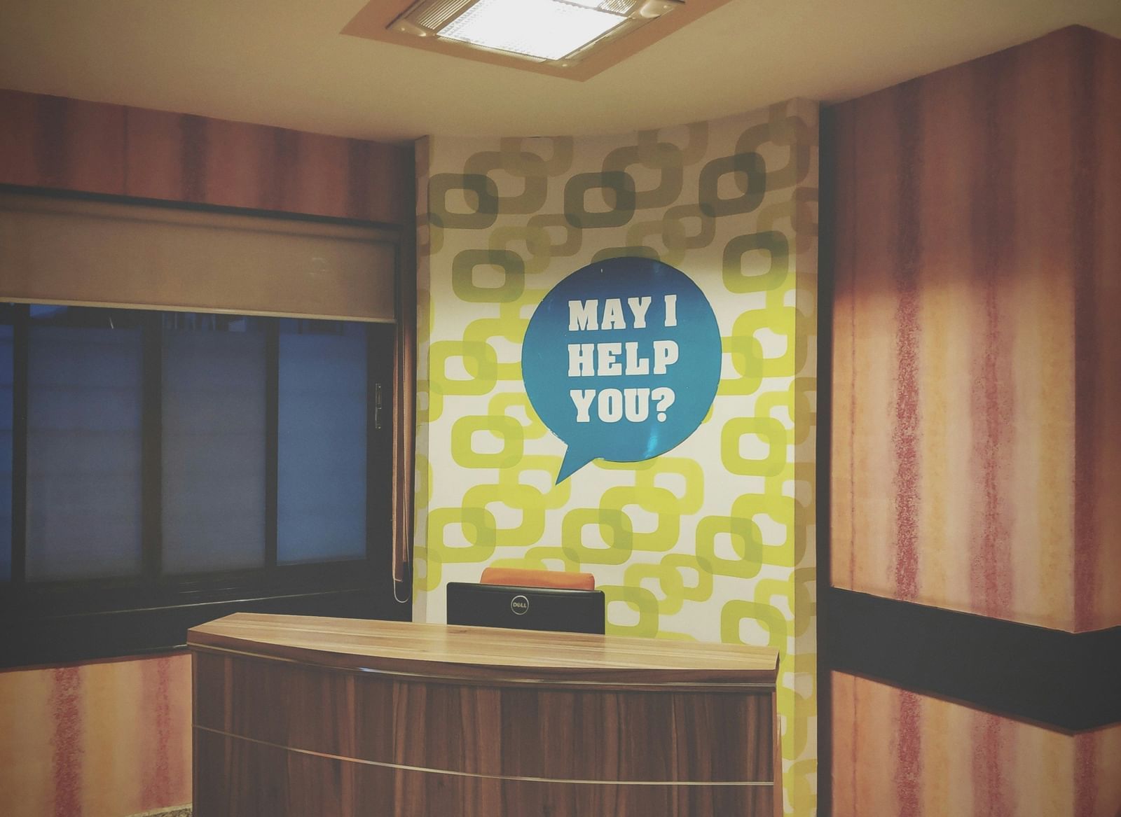 A reception desk with a quote in the background asking 'May I Help You'?
