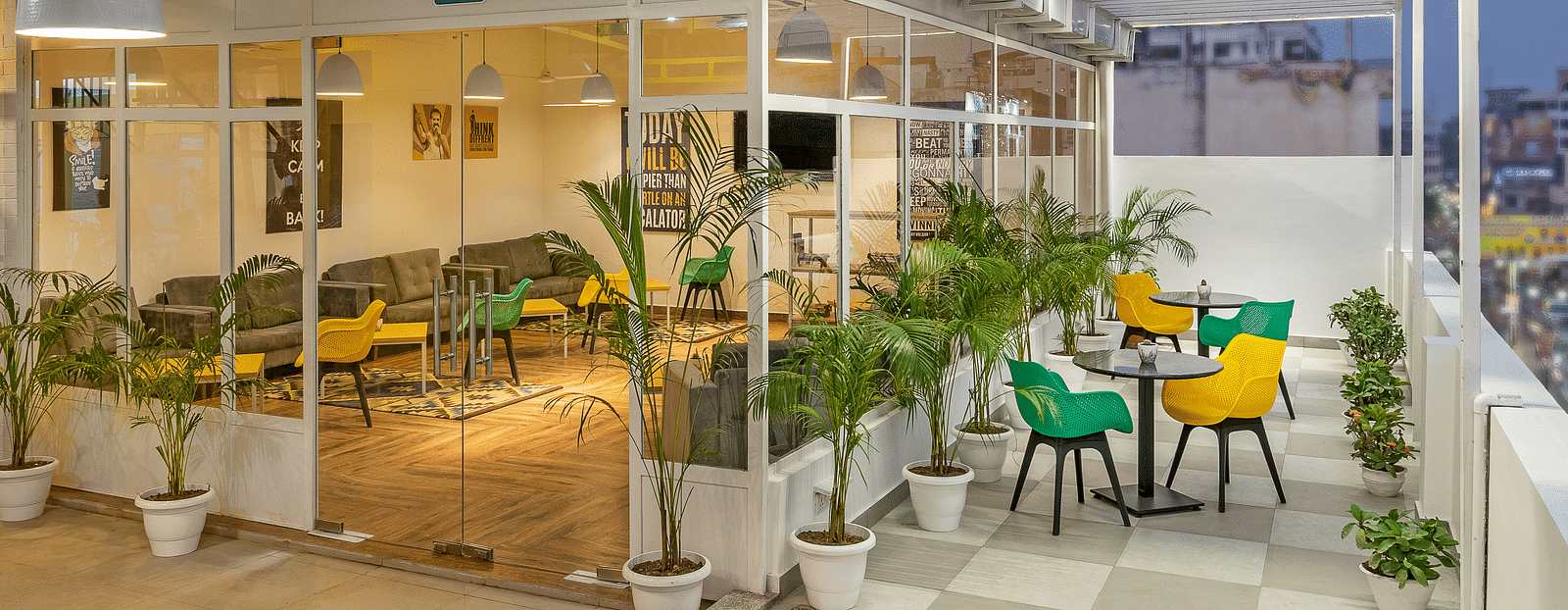 An image of a lounge featuring both indoor and outdoor seating,  with a few plants outside, beautifully lit for the evening atmosphere.