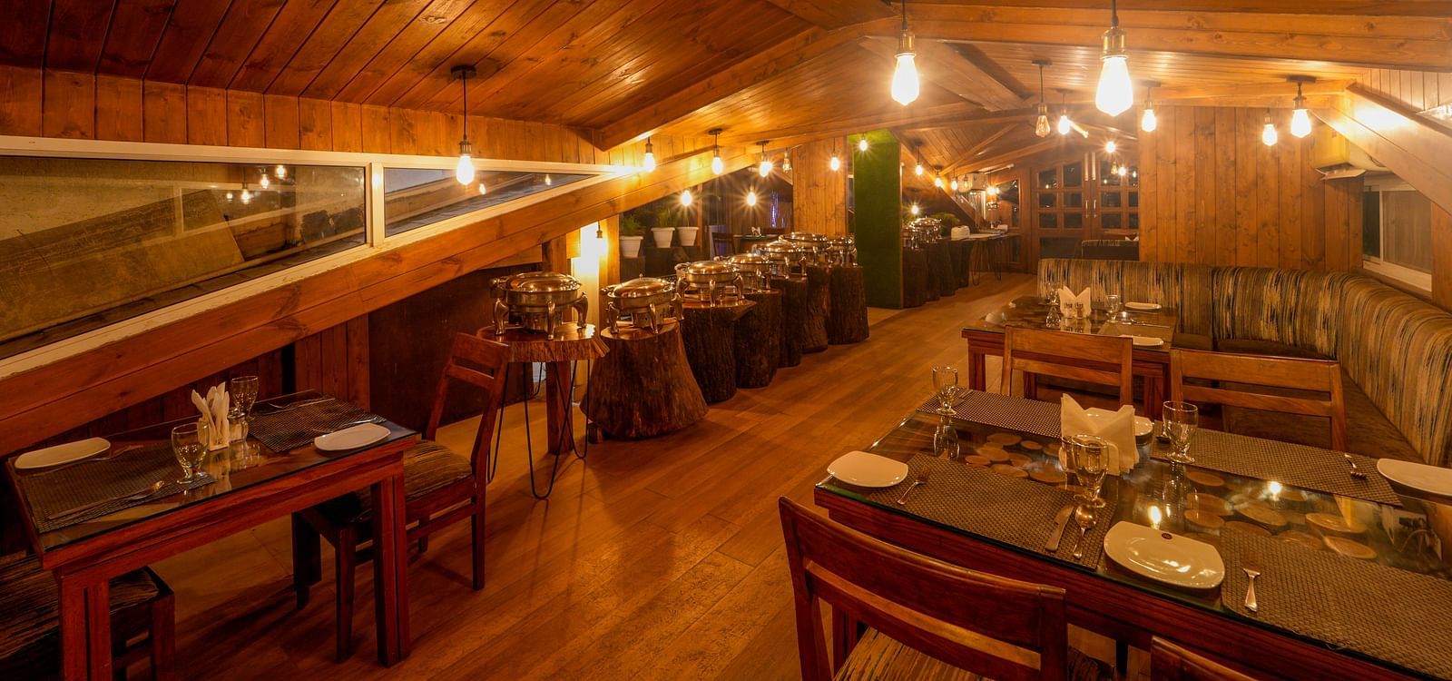 The wooden interiors of the restaurant at DLS Whispering Winds with chairs and tables which it lit with bright lighting