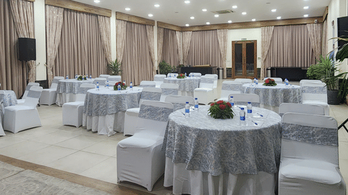 Elegant event hall with round tables covered in patterned tablecloths, white chairs, floral centerpieces, and soft overhead lighting - Suryavilas Luxury Resort and Spa