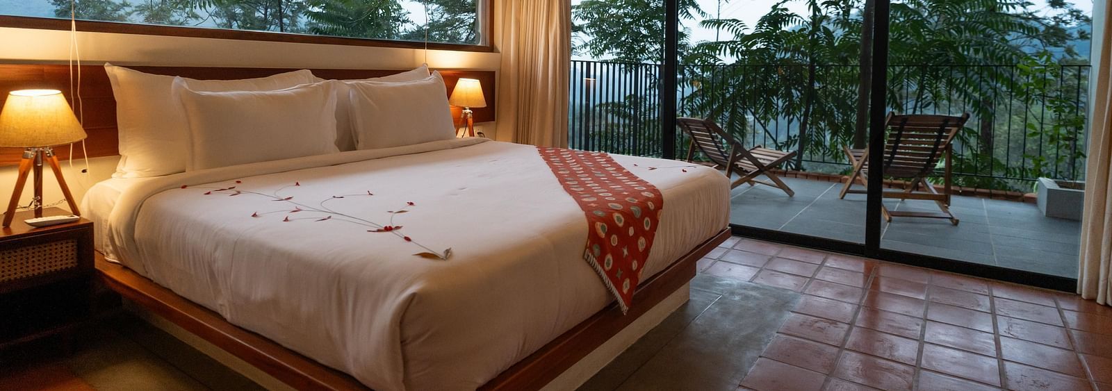  A well-appointed bedroom at Vaasta Vagamon featuring a large bed with a decorative runner, and expansive windows overlooking a scenic view.