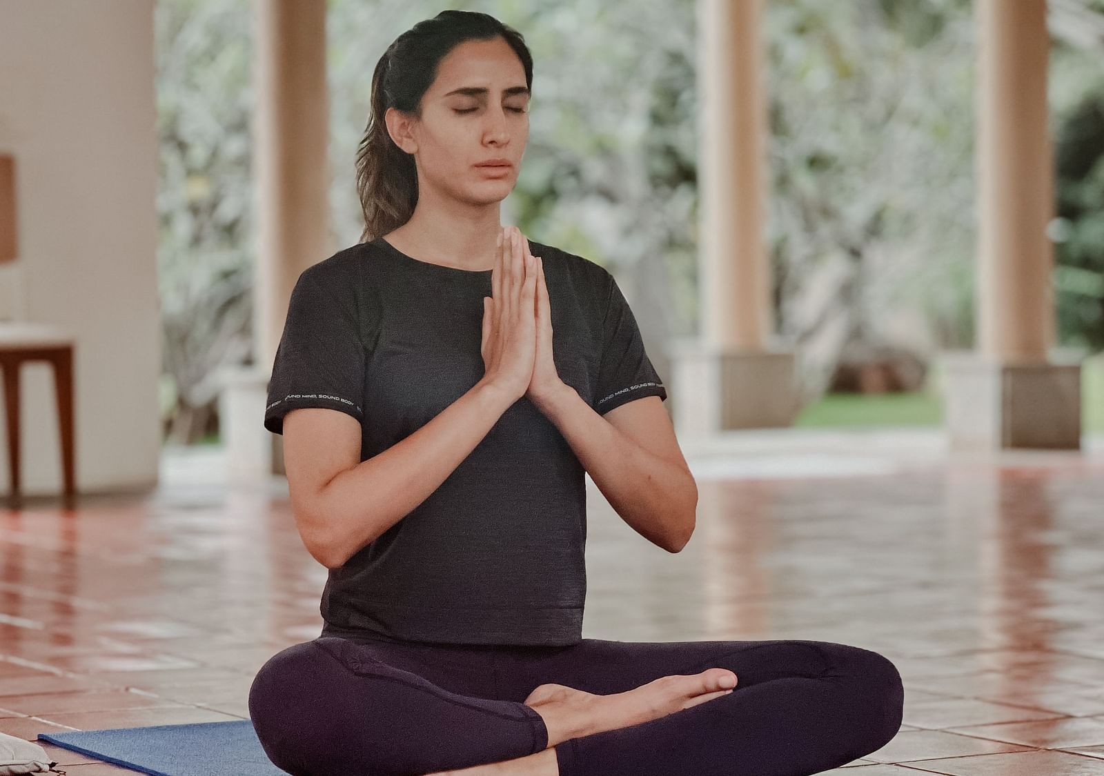 A person doing yoga on a mat in a room with large windows and plants.