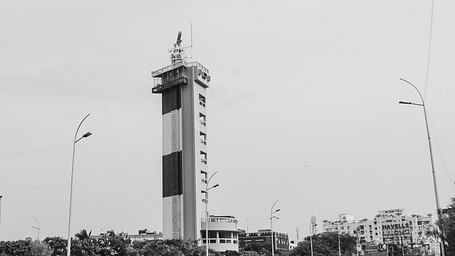 An overview of a light house in Chennai with bikes riding on the road next to it.