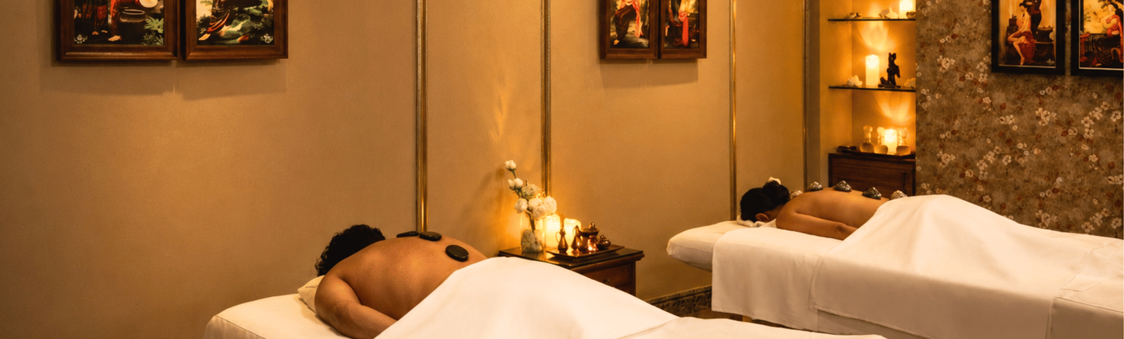 Two people receiving a hot-stone massage on side-by-side beds in a candlelit spa room at MAYFAIR Palm Beach Resort, Gopalpur-on-Sea.