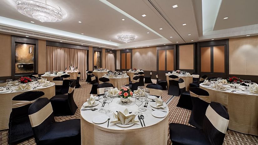 Banquet hall with round tables set for a formal event, featuring chandeliers and high ceilings.