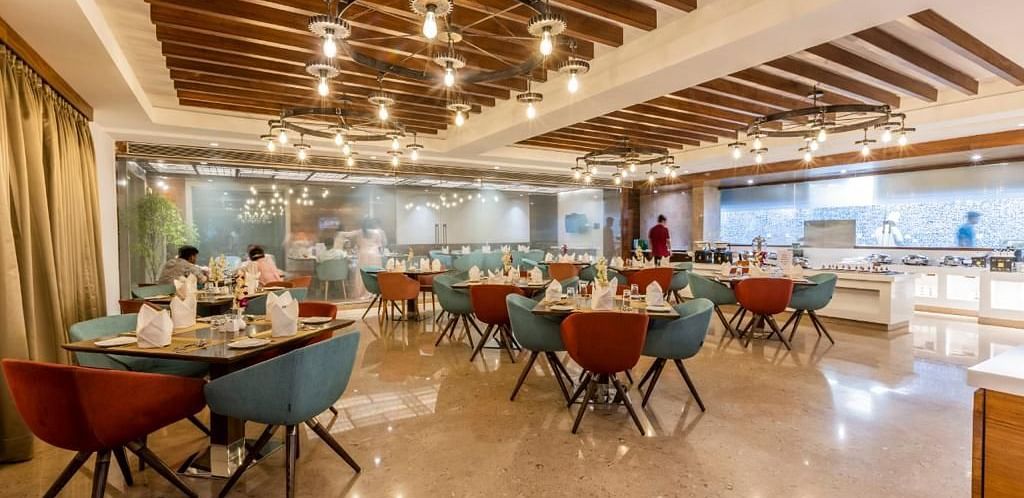 Warmly lit dining area at Rang Lords Inn, with a wooden beamed ceiling, modern chairs, and set tables, ready for a meal