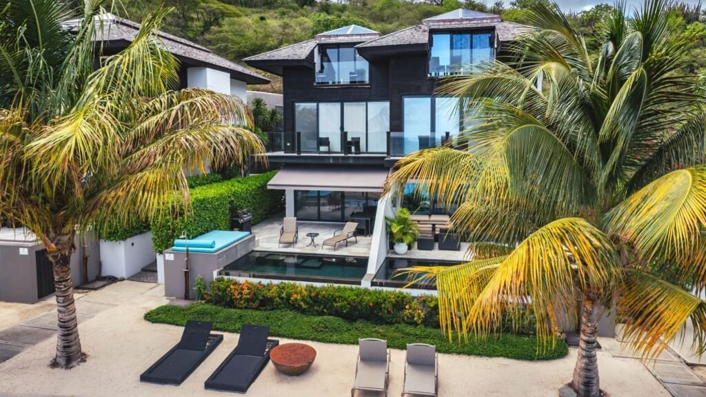 A wide angle shot of the villa with cars parked and trees all around.