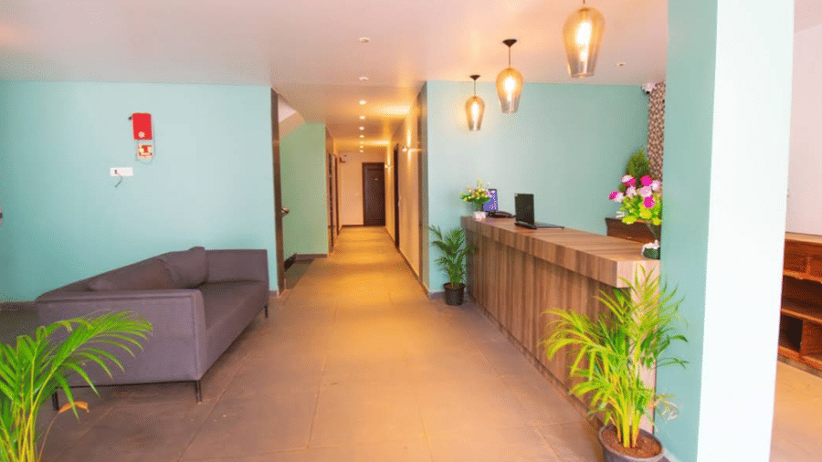 A reception lobby featuring a wooden desk, a grey sofa, and light green walls at Estherea Elite, Morjim.