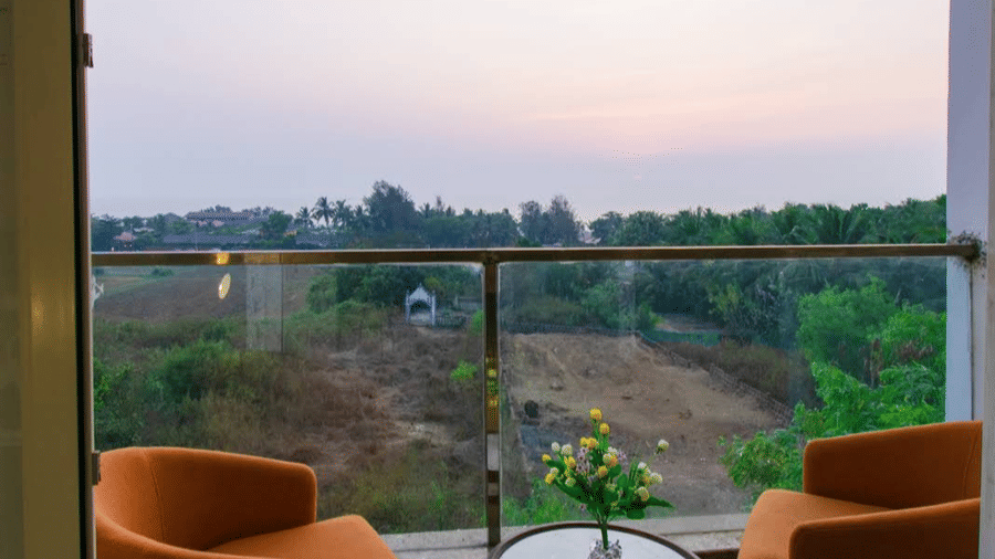 A balcony with 2 orange chairs and a small table overlooks a field and trees at Estherea Elite, Morjim.