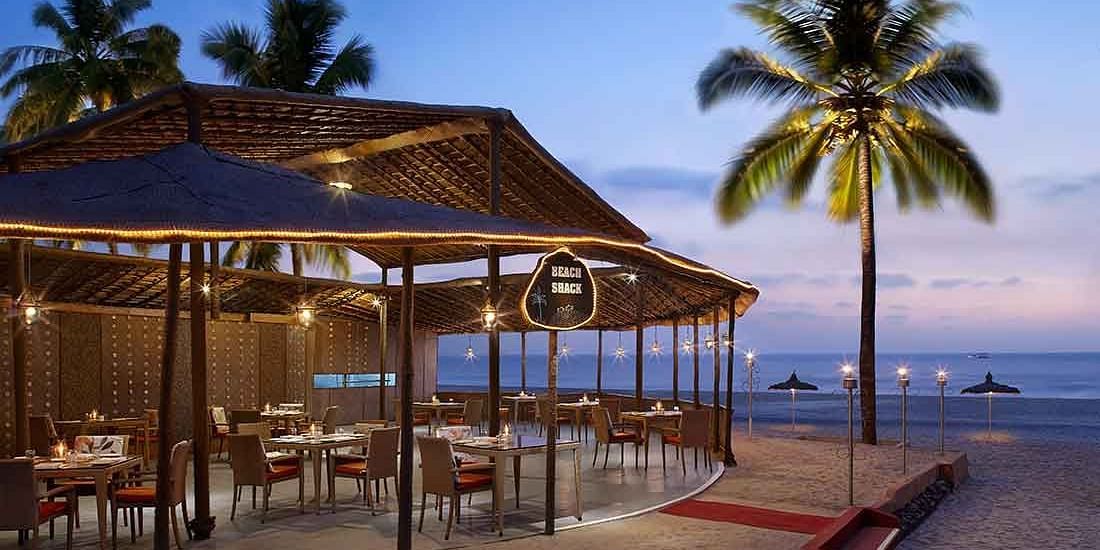 An inviting beachside restaurant with open-air seating, illuminated warmly as the evening sets in, creating a perfect dining ambiance by the sea.